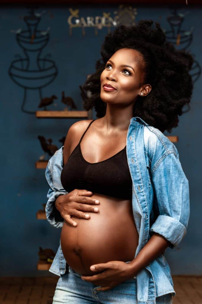 Black pregnant woman in a jean shirt holding her stomach