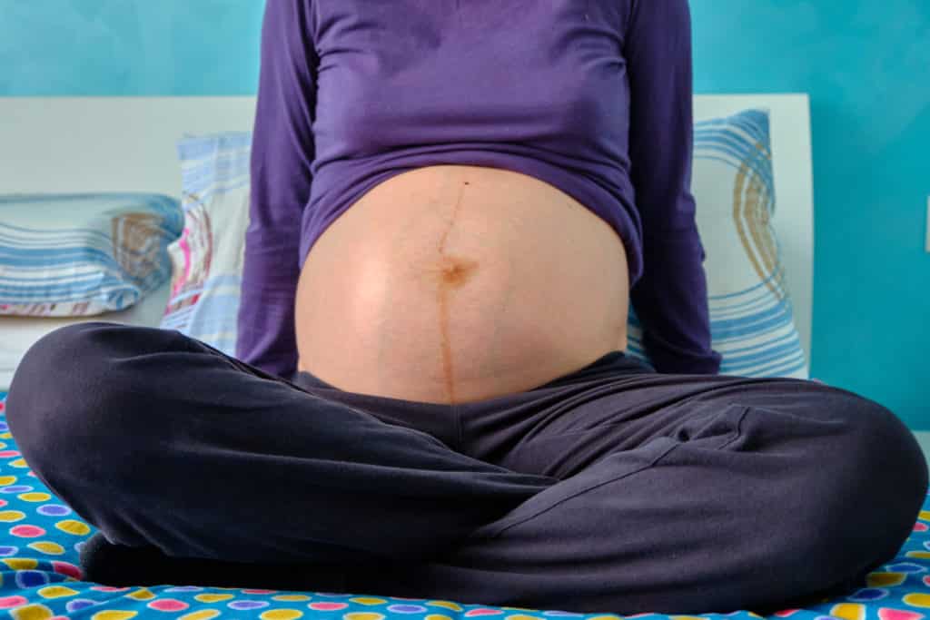 A woman sitting and showing her pregnant stomach 